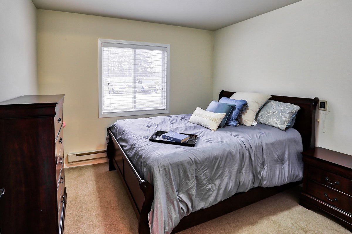 A cozy bedroom with a neatly made bed and pillows near a window.