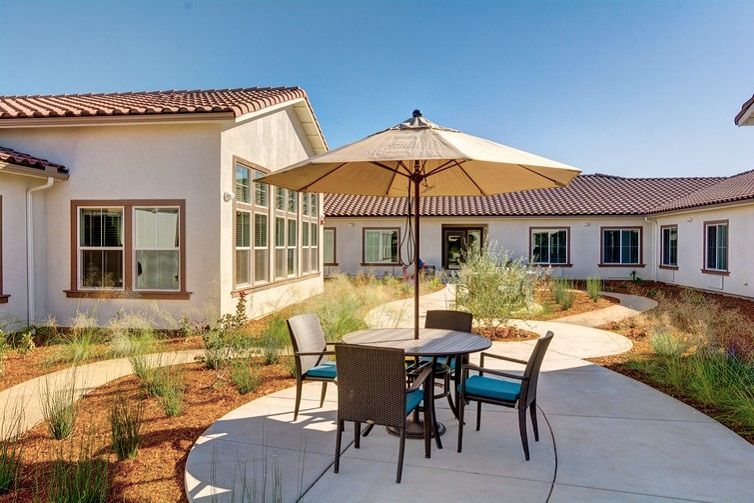 A sunny patio area with a table, chairs, and an umbrella beside a modern building.