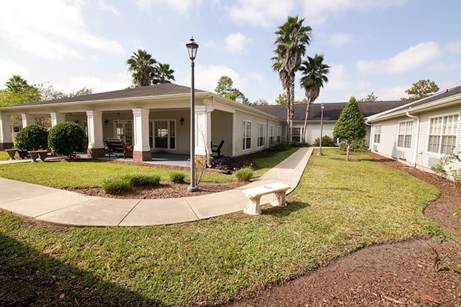 A peaceful outdoor area featuring a pathway leading to a building, surrounded by palm trees and greenery.
