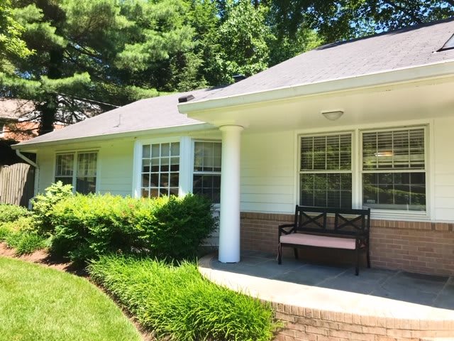 A cozy house with a front porch, featuring a bench and surrounded by lush greenery.