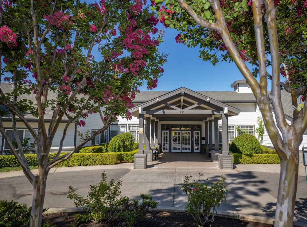 A well-maintained building entrance surrounded by lush landscaping and blooming trees.