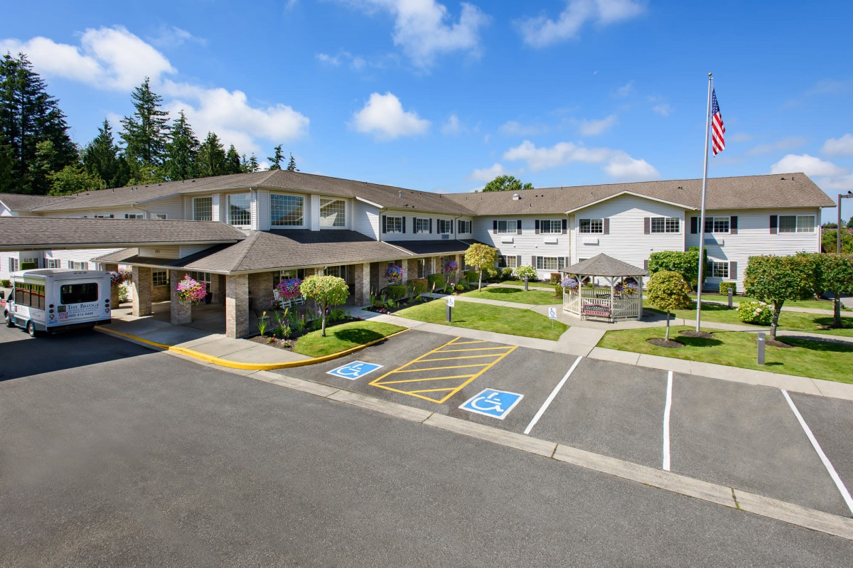 A large residential building with a landscaped parking area on a sunny day.