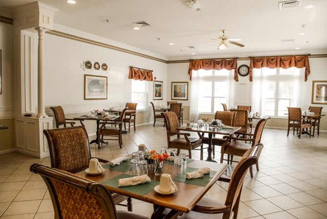 A cozy dining area with neatly arranged tables and chairs, featuring warm decor and large windows.