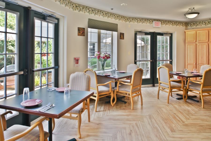 A bright and inviting dining area with several tables and chairs arranged near large windows letting in natural light.