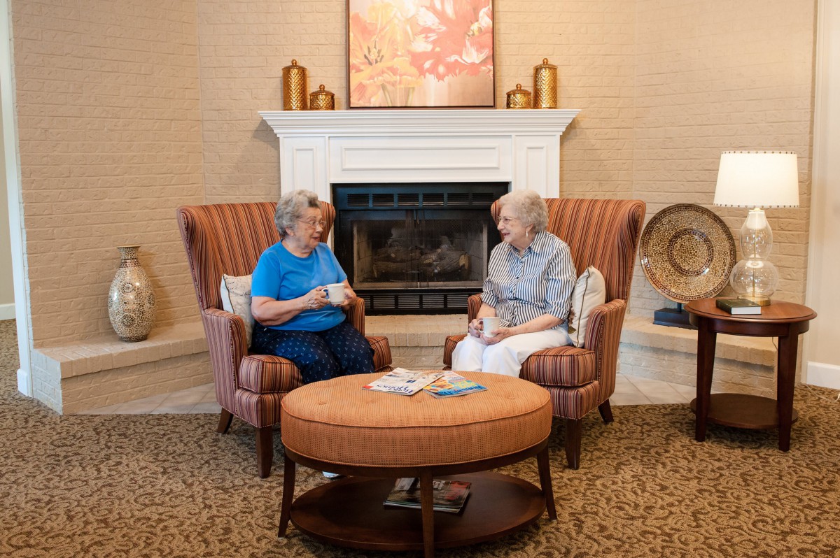 Two seniors having a conversation over coffee in a cozy living room setting.