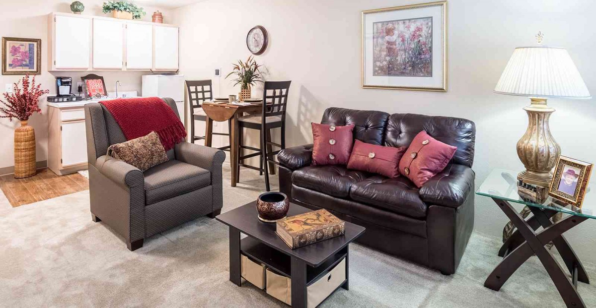 A cozy living room with a sofa, armchair, and coffee table, adjacent to a small dining area.