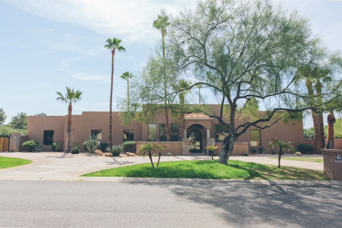 A desert-style house with palm trees and a lush front yard on a sunny day.
