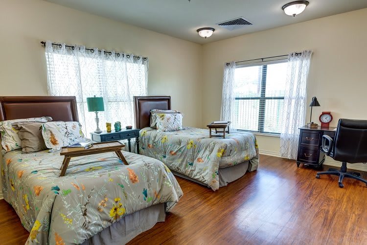A cozy bedroom with twin beds, featuring ample natural light and warm wooden flooring.