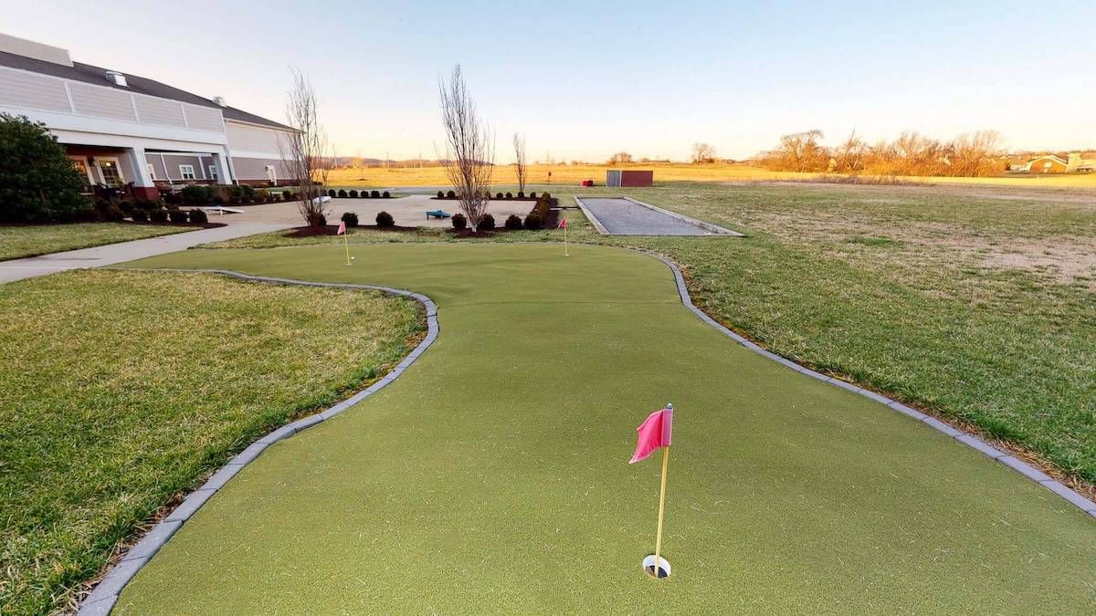 A well-maintained outdoor putting green with a bright red flag set against a clear sky.