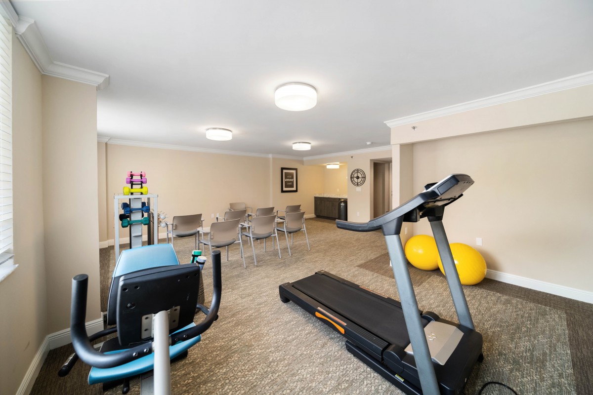 A small gym with a treadmill, stationary bike, exercise balls, and chairs in a carpeted room.