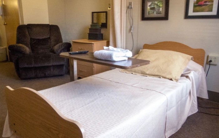 A hospital room featuring a neatly made bed with a bedside table and towel.