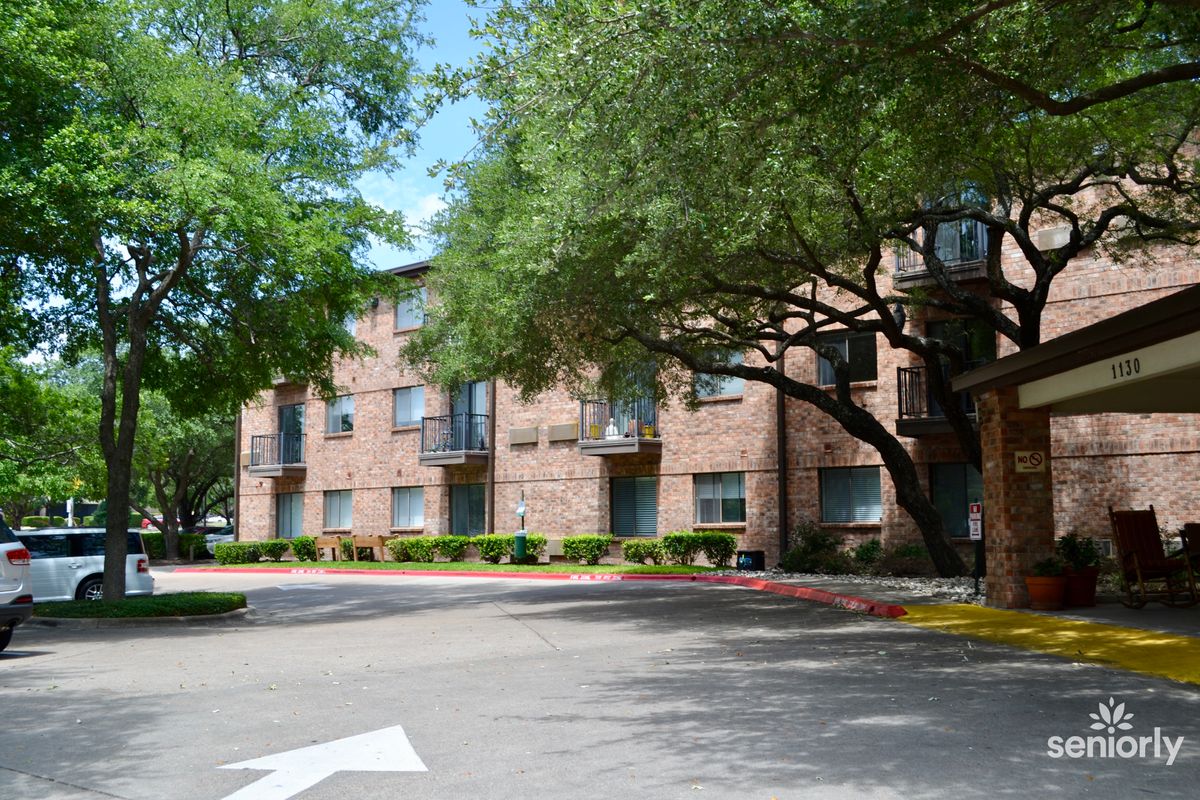 A view of a brick apartment building surrounded by trees with a parking lot in front.
