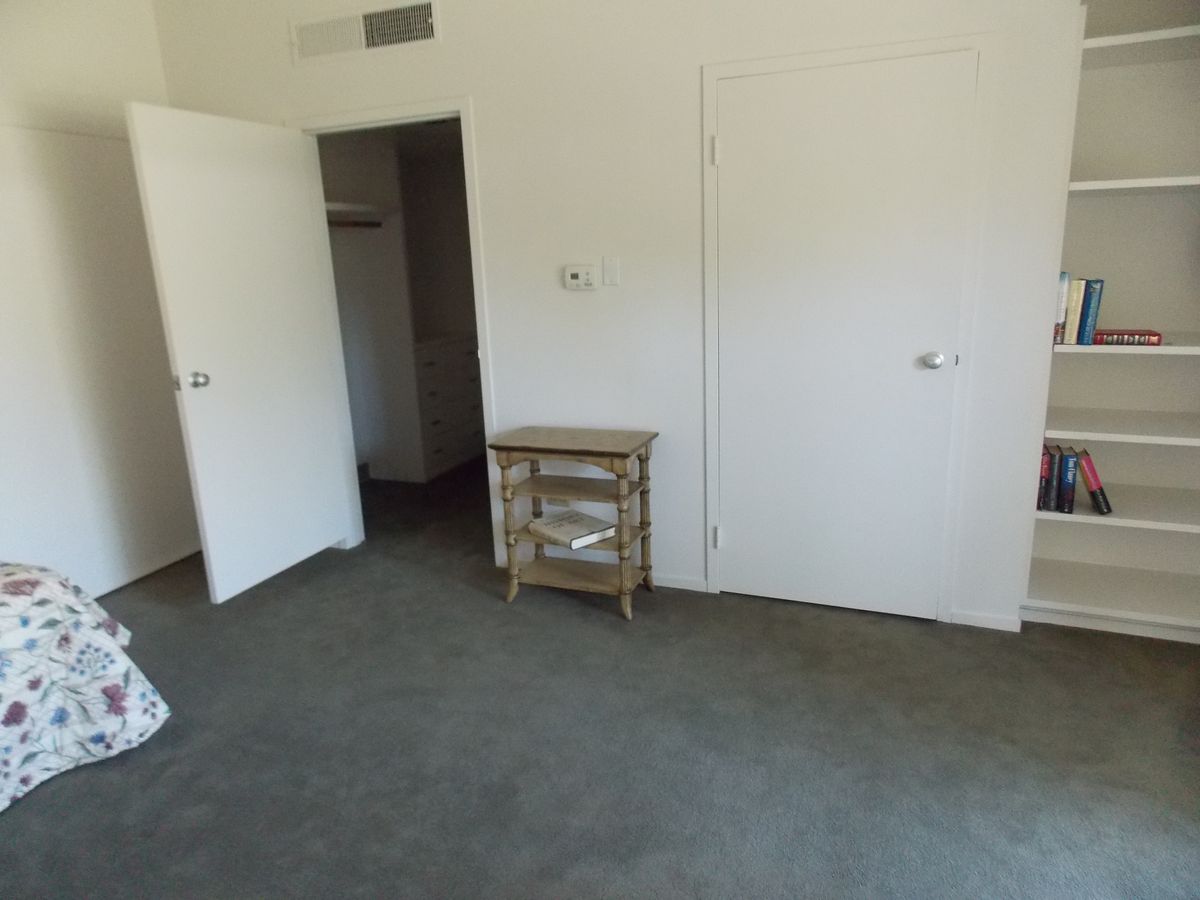 An empty room with a carpeted floor, featuring a small dresser and an open door.