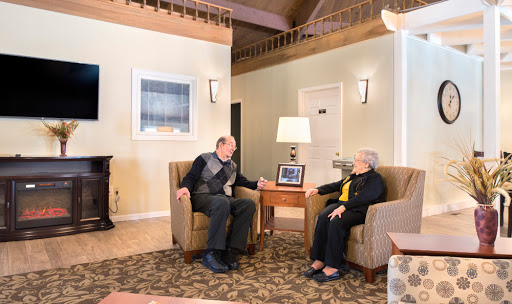 An elderly man and woman engage in a warm conversation while using a tablet in a cozy living room setting.