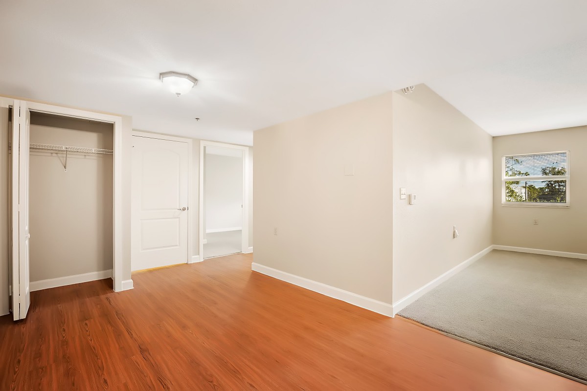 A clean, empty room with wood flooring and a hallway leading to doors.