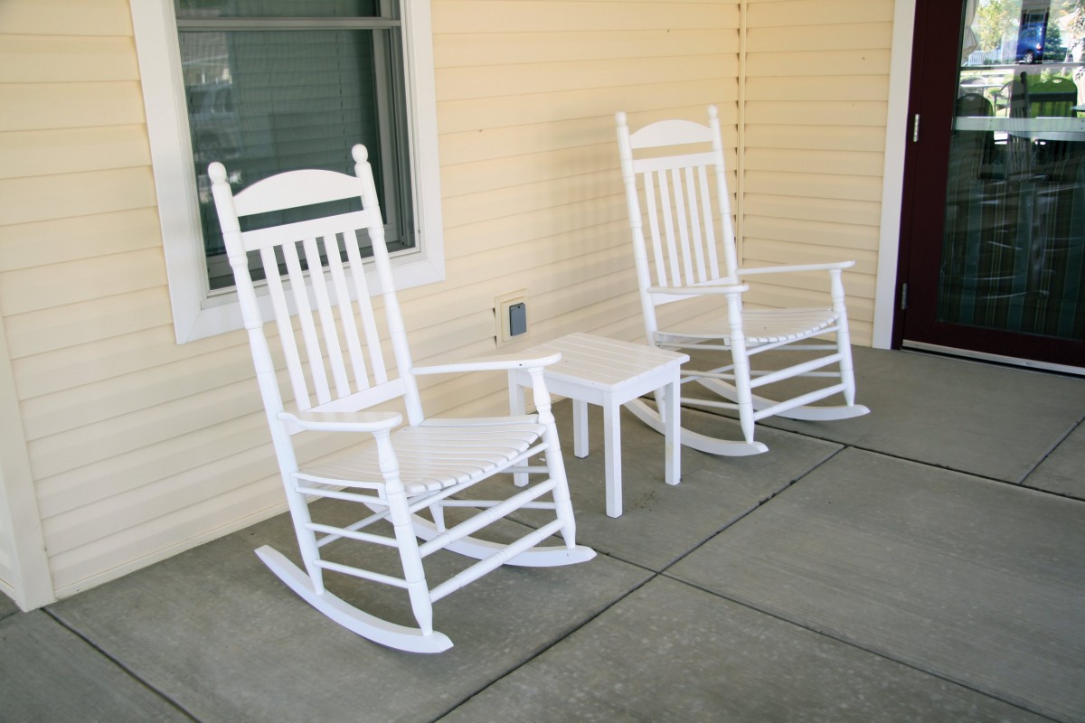 Two white rocking chairs and a small table on a porch.
