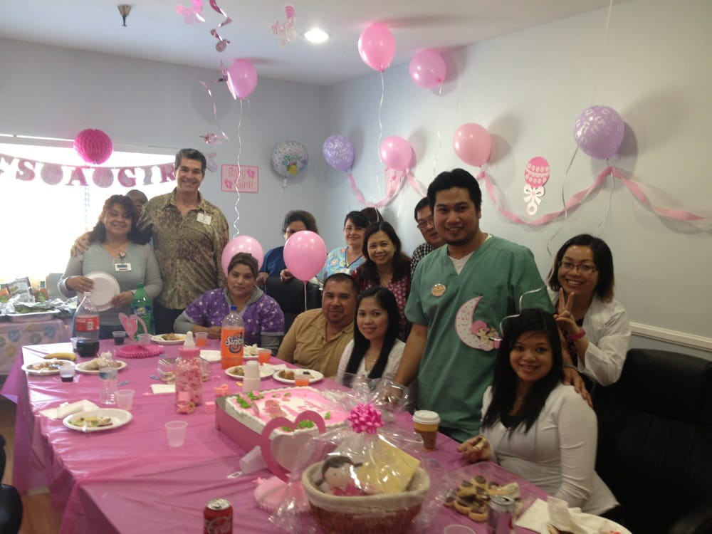 A group of people celebrating a baby shower with pink decorations and balloons.