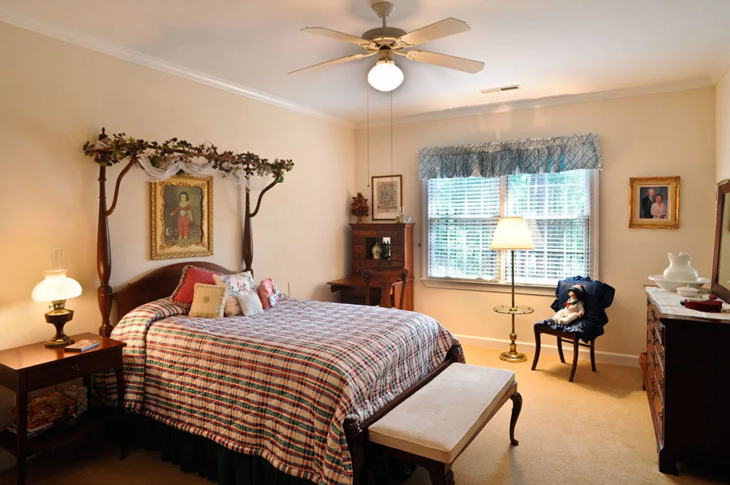 A cozy, traditionally decorated bedroom with a ceiling fan and natural lighting.