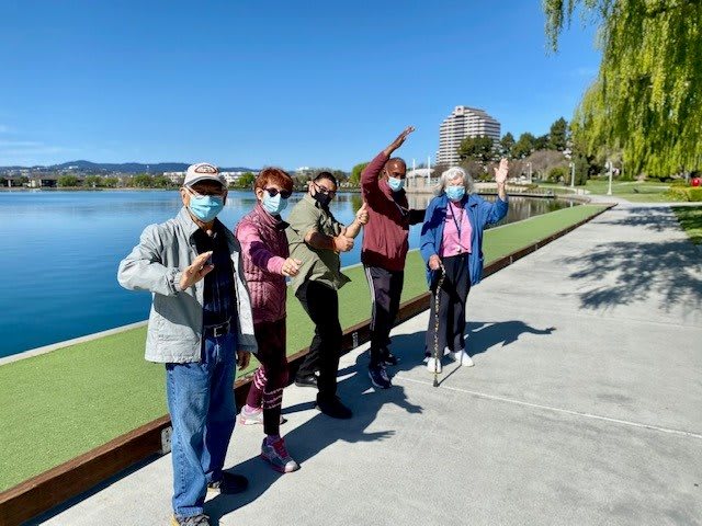 A group of people wearing masks enjoying a sunny day by the lake.