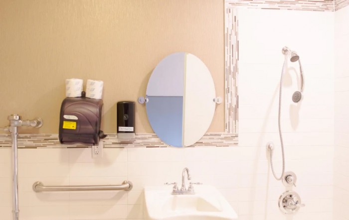 A modern bathroom featuring an oval mirror, sink, and wall-mounted amenities.