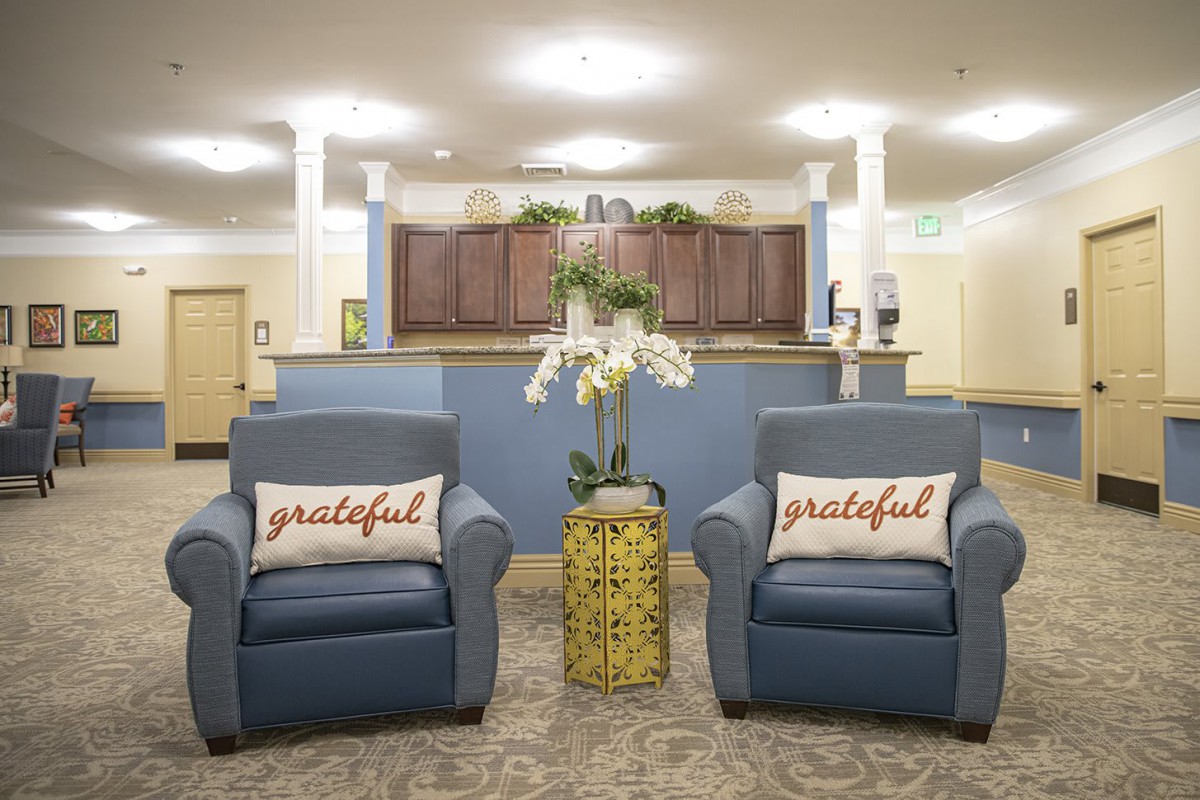 A cozy lobby area with two blue chairs, each adorned with a 'grateful' pillow and a decorative flower arrangement in between.