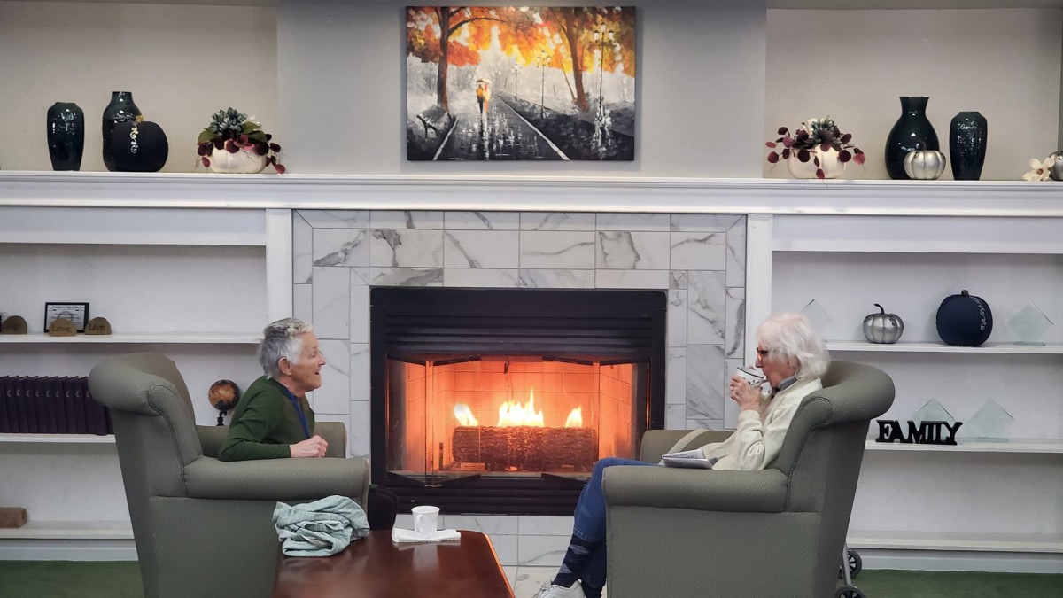 Two people enjoying a conversation by the warm fireplace in a cozy living room setting.