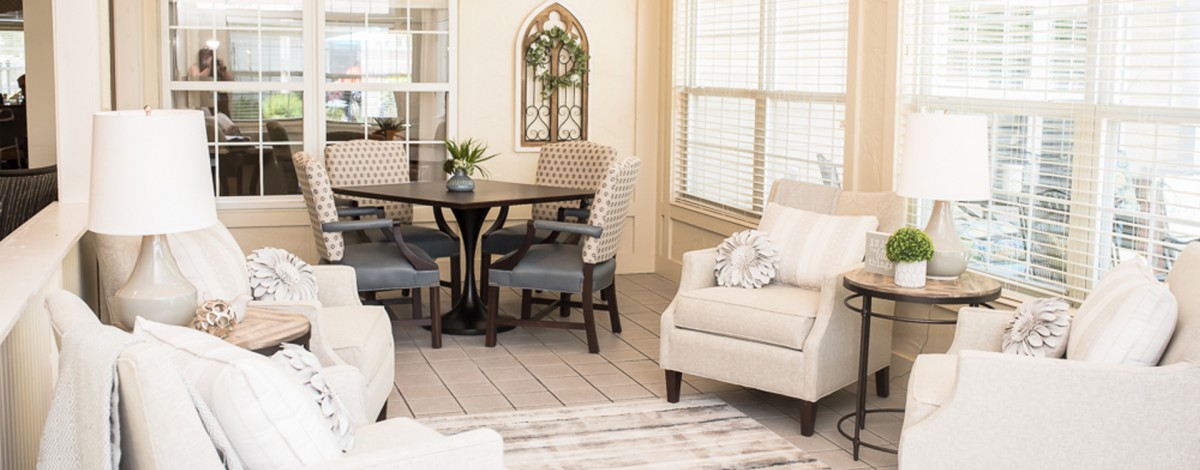 A cozy living room featuring a dining area with a round table and chairs, an armchair, and decorative elements including plants and window blinds.