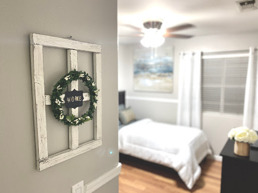 A cozy and stylish bedroom featuring a decorative wreath on the wall and a neatly made bed, illuminated by natural light.