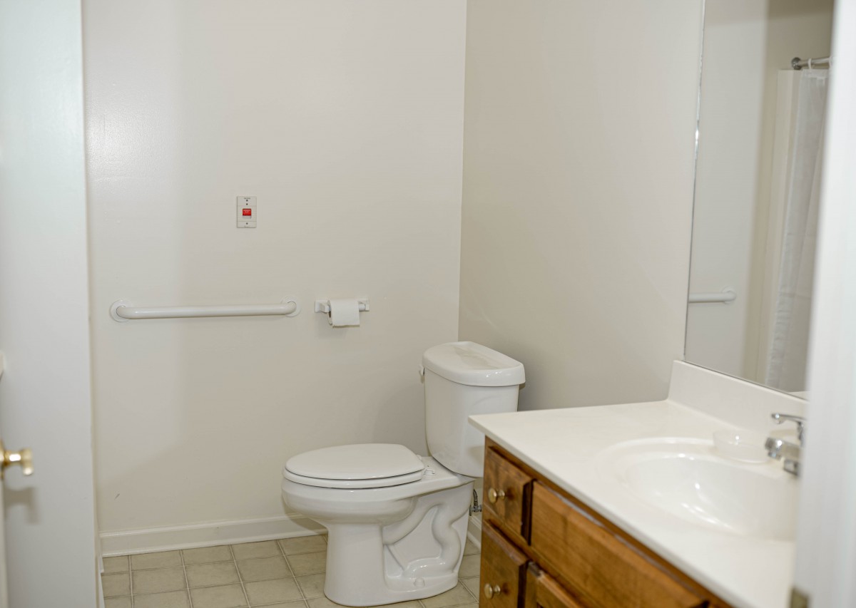 A clean bathroom featuring a toilet, sink with a wooden cabinet, and a mirror.