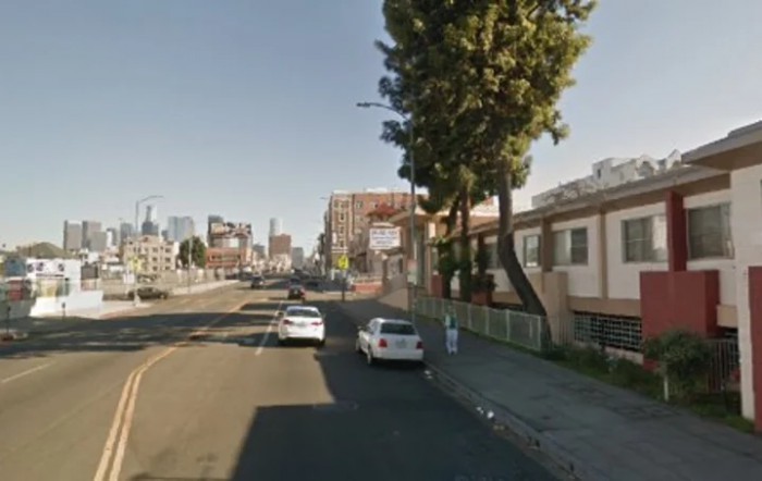An urban street scene with parked cars and buildings under a clear sky.