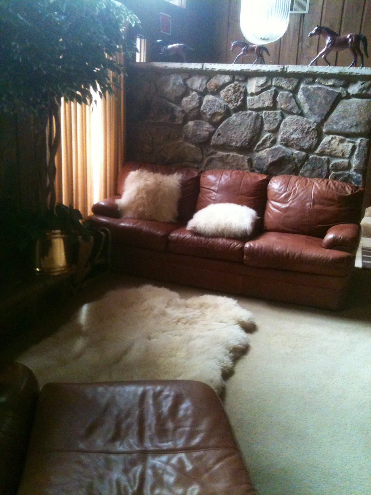 A cozy living room with a leather couch and stone wall.