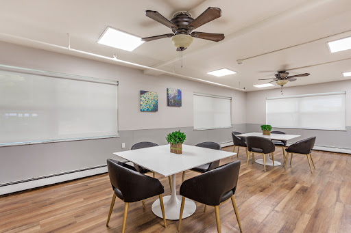 A modern meeting room equipped with comfortable chairs, tables, and ample natural light.