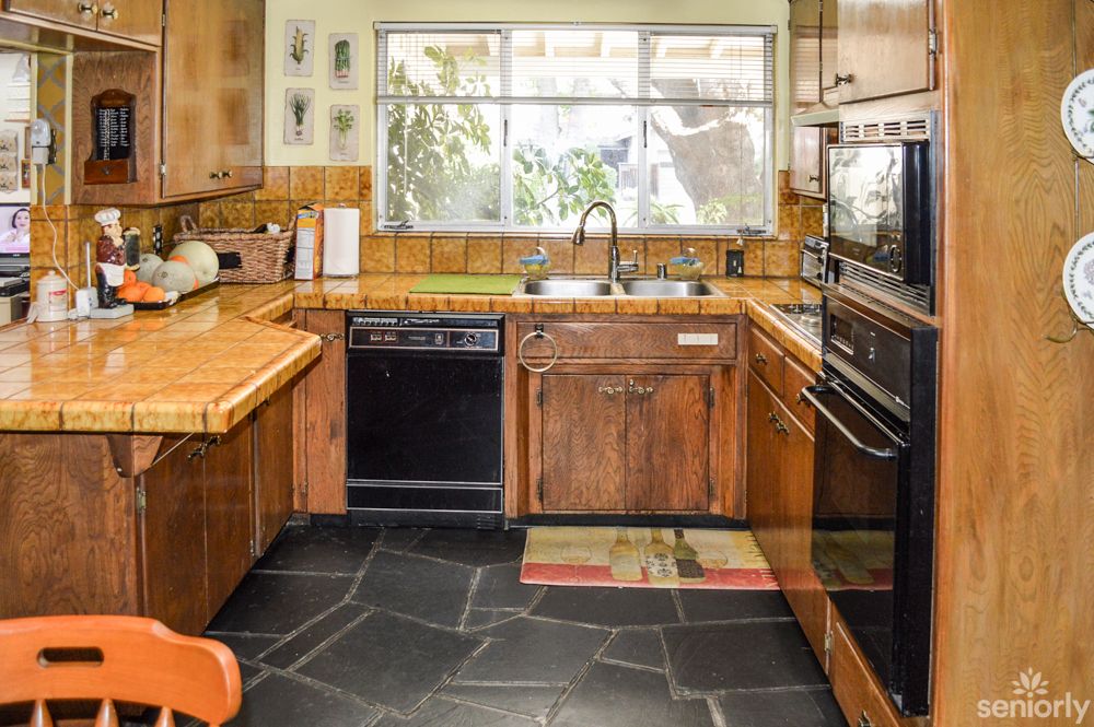 A cozy kitchen interior featuring wooden cabinets, a dishwasher, an oven, and a large window.