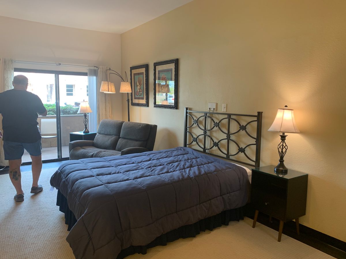 A cozy bedroom featuring a bed with a dark comforter, a sofa, and ambient lighting from lamps.