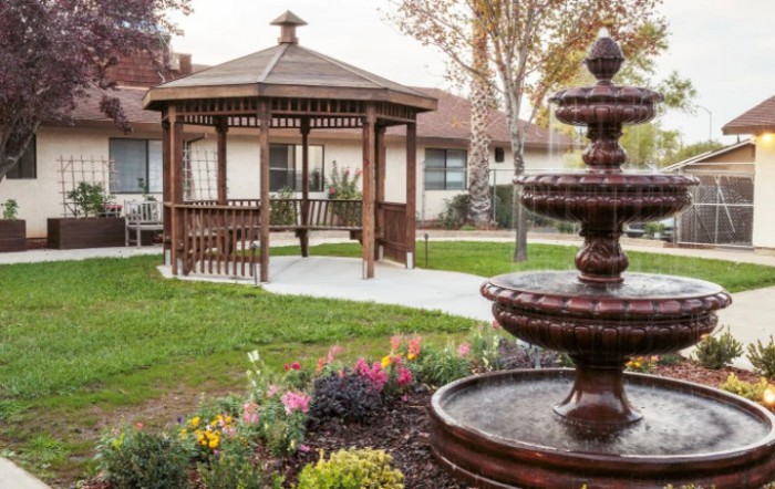 A serene garden scene featuring a wooden gazebo and a tiered fountain surrounded by flowers.