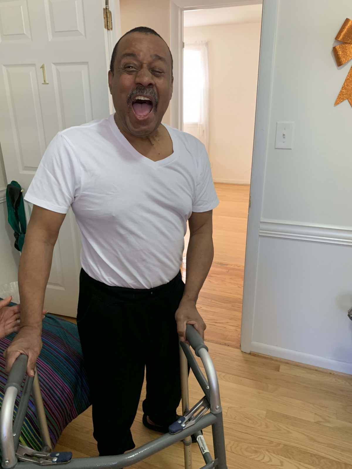 A man smiling indoors while using a walker.