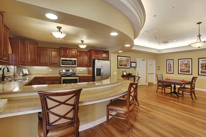 A modern kitchen with wood flooring and stainless steel appliances, featuring a curved bar and dining area.