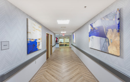 A modern hospital hallway featuring artwork on the walls and clean oak flooring.