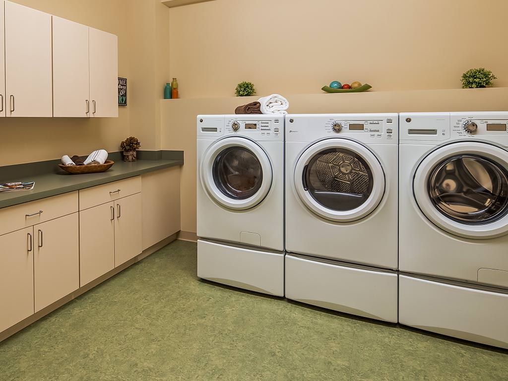 A clean and organized laundry room with three front-loading washing machines and cabinetry.
