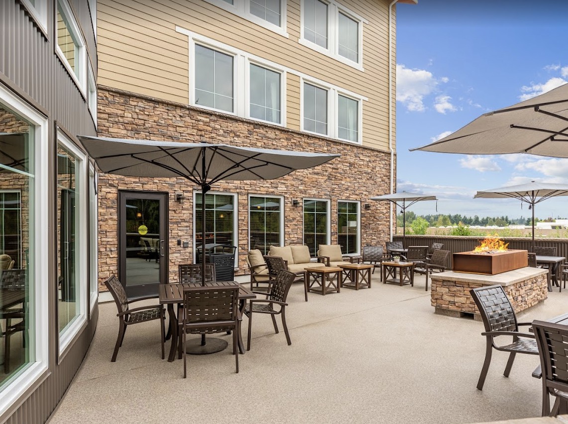 A comfortable outdoor patio with tables, chairs, and umbrellas, adjacent to a building under a clear blue sky.