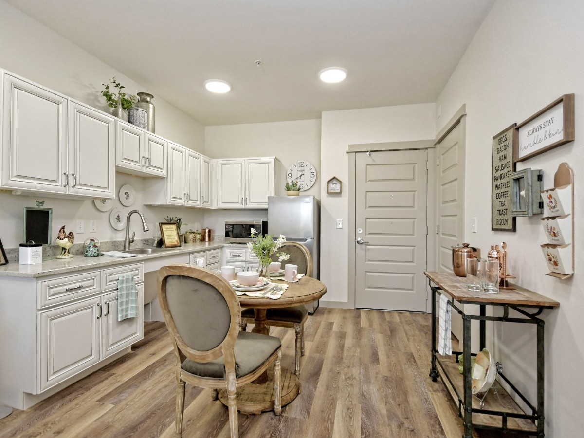 A modern kitchen with white cabinets, wood flooring, and a cozy dining area.