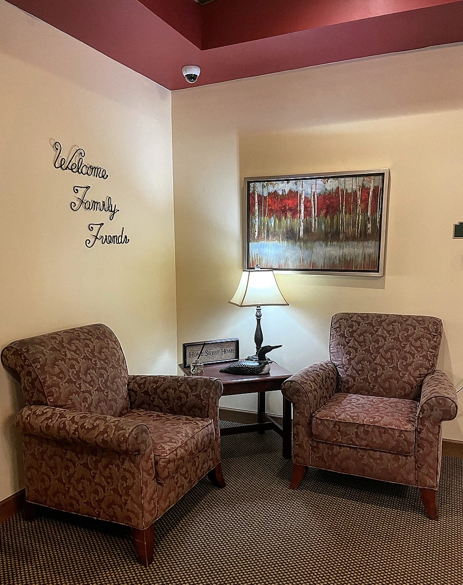A cozy waiting room with two upholstered chairs, a lamp on a side table, and decorative wall art.