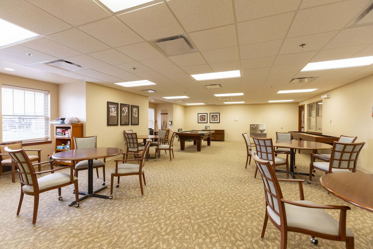 An interior view of a well-lit room with multiple tables and chairs arranged on a carpeted floor.