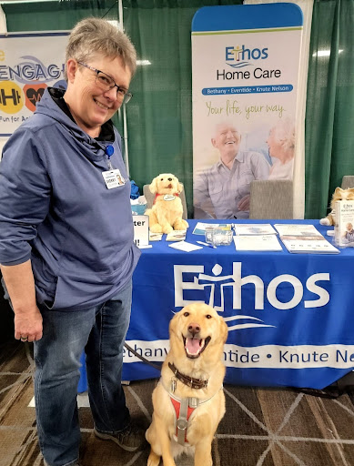 A person and a golden retriever dog at a home care booth, both looking cheerful.