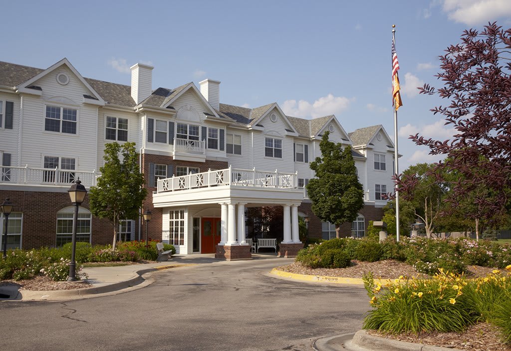 A large residential building with a landscaped entrance and flagpole on a sunny day.