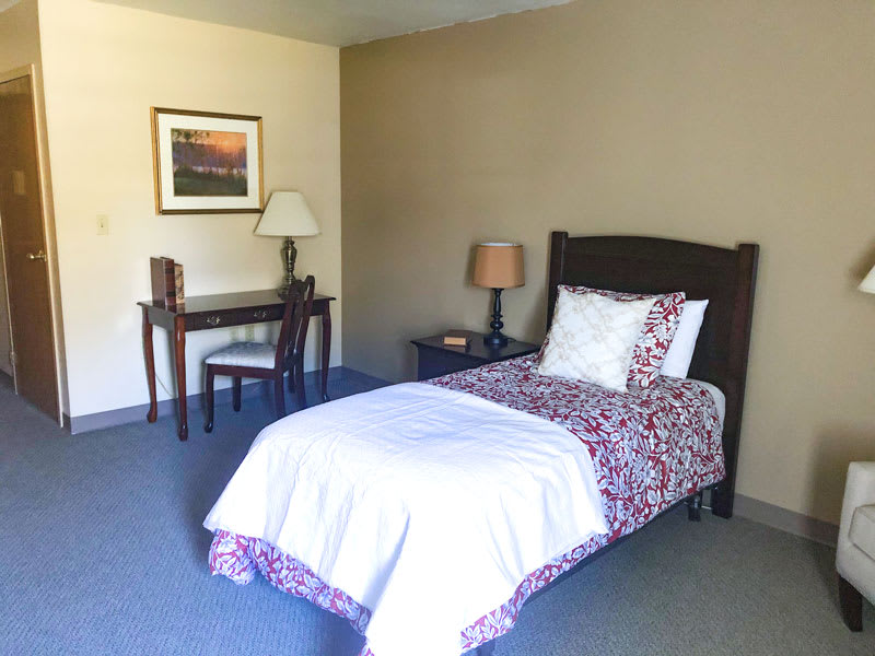 A minimalist bedroom featuring a single bed, desk, chair, and lamp.