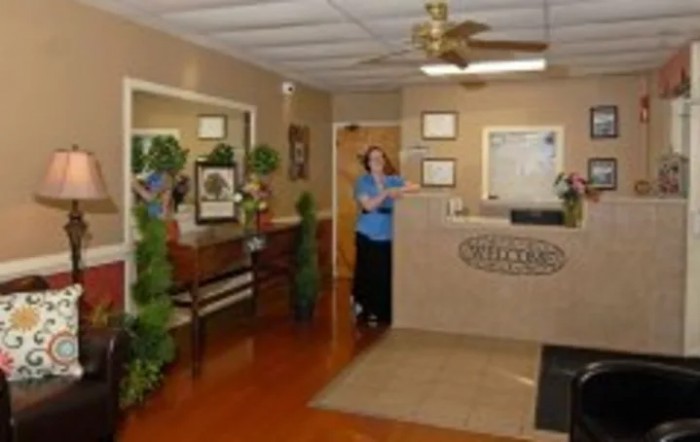 A reception area with a desk, plants, and a woman standing near the counter.
