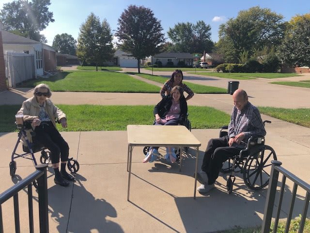 A group of people sitting in wheelchairs around a table outdoors on a sunny day.