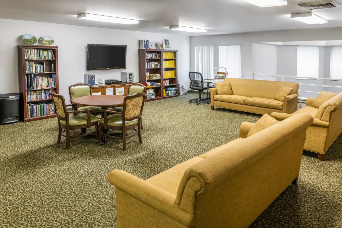 A cozy living room featuring sofas, a TV, shelves, and a round table with chairs.