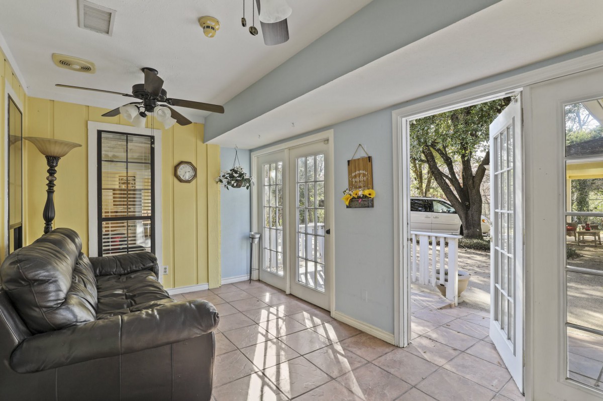 A bright living room with glass doors leading to an outdoor area, featuring a ceiling fan and tiled flooring.